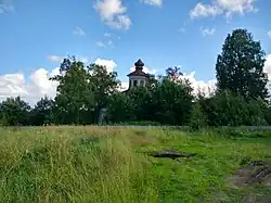 A photograph of the church of St. George the Victorious obscured by green trees, with grass in the foreground.