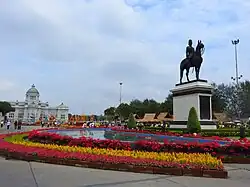 A large plaza with a bronze statue of a man riding on horseback; beyond the plaza is a large two-storey building with a domed roof, arched windows and columns