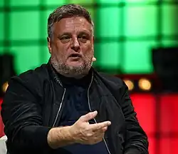 A man faces the camera, he is wearing a portable microphone