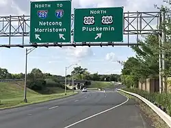 A multilane highway in a suburban area at a split, with two green signs over the road. The sign on the left reads north Interstate 287 to Interstate 78 Netcong Morristown with an arrow pointing to the upper right and the sign on the right reading north U.S. Route 202/U.S. Route 206 Pluckemin.
