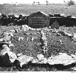 A grave site marked with white rocks and two headstones, in front of a low rock wall