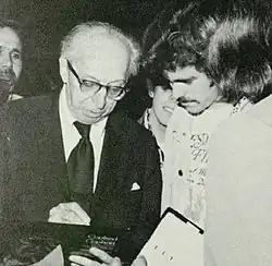 Man wearing glasses and a suit on the left next to another man