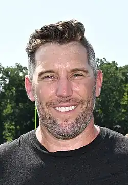 Closeup photo of a man in a black t-shirt smiling outside on a sunny day.
