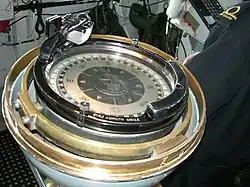 a colour photograph of a large compass surrounded by a brass ring installed on the bridge of a ship