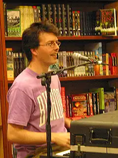 A bespectacled Andy Creegan, playing a keyboard at a library