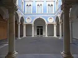 A courtyard of classic renaissance design in blue with white columns and roundels and windows on the second level