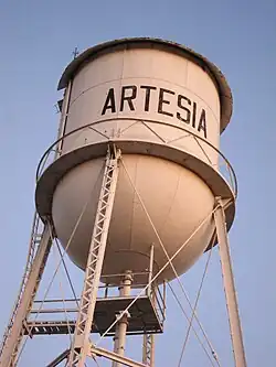 Water tower with Artesia written across it. Picture is taken from below and shows only a cloudless sky in the background