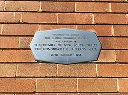 A stainless steel plaque on a brick wall, located at Ashfield Pool, opened by NSW Premier, R.J. Heffron, 26 January 1963.