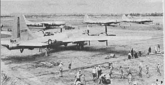 Four large 4-engined World War II–era aircraft sitting on the ground at an airstrip. Groups of people are working near each aircraft.