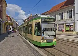 A cream and green low-floor tram in a cobbled street