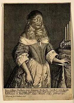 A three-quarter length portrait of a woman standing with her hand on an organ. The woman has long hair flowing from her face and wears 17th century clothes: a corseted dress and apron.