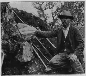 William E. Hidden next to a 73 lb (33 kg) mass of gadolinite in place at Barringer Hill, 1903.