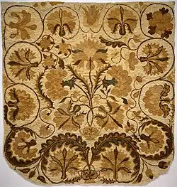 The rug is rounded at one end, and the motif is large flowers, with those in the center forming a bouquet growing from a small urn.
