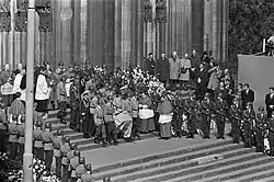 A black and white photograph of multiple uniformed people walking at a funeral procession