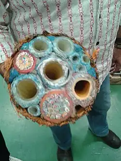 A man holds the cut face of a small section of bell umbilical to the camera. The cut ends of various component hoses and cables can be seen bound together by a braided yellow cover