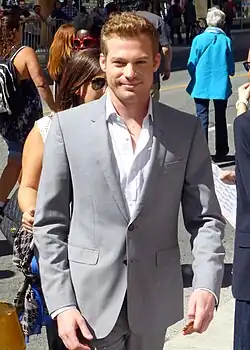 Reid in grey suit, smiling to the camera
