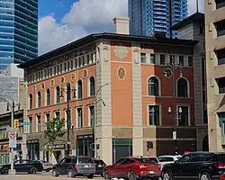 Four storey terracotta coloured building with ornate designs, including an ornate "B" in a tall octagon shape.