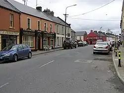 Small village street lined with houses, pubs and parked cars.