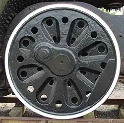 An almost solid disc (not spoked) locomotive wheel with a series of cast-in radial indentations and prominent round holes intended to reduce its weight.