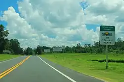 A road with a sign with text "Orchard Pond Parkway: SunPass or toll-by-plate"