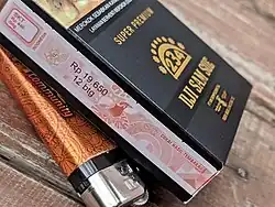 Box of Dji Sam Soe Premium cigarettes sitting on the table, with the warning partially seen and the tax stamp fully seen. Under the box is the lighter.