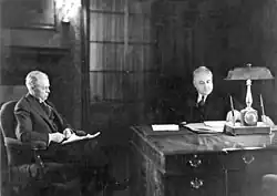 A black and white image of the Van Sweringen brothers. One sits behind a desk, the other in a chair to the left