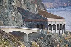 A highway bridge leads to a rock shelter protecting the roadway from rocks falling off the cliff above.