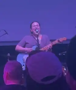 Carmen Perry standing and singing while playing guitar.