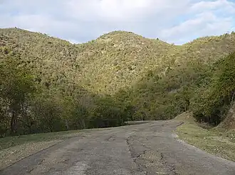 photo of a paved road, with crumbling pavement, and 3 hills in the distance