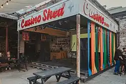 A photograph of a stage surrounded by colourful streamers with vintage style red text that says Casino Shed