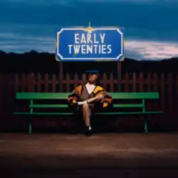 Burns sitting on a green bench in front of a fence looking up at a blue sign that reads "Early Twenties".