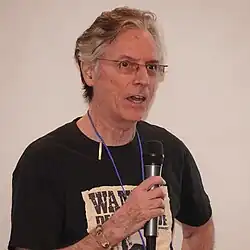 Charles Pellegrino wearing a black print t-shirt, speaking into a microphone