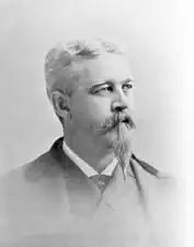 Photograph of man in a dark suit with a large white goatee