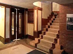 A staircase in the house. The ceiling above the staircase has a curved opening. There is a double door with glass panes to the left.