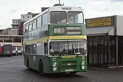 Green, yellow and white double-decker bus leaving a bus station