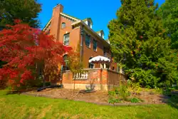 This Colonial Revival house features a porch with balusters, a doorway surrounded by engaged columns supporting a lintel and entablature with faux balcony, and arched windows.