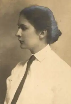 A young white woman with dark hair dressed to the nape, wearing a collared white shirt and a dark necktie