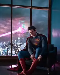 Image of David Corenswet suiting up as Superman while an alien-looking threat attacks in the background