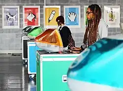 A visitor browses a website on an iMac G3 with Susan Kare prints in the background