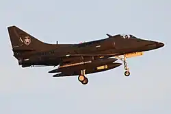 Colour photo of a green military jet aircraft in flight with its landing gear extended