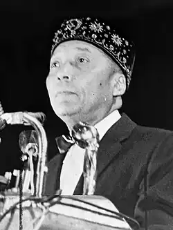 Black-and-white photo of Elijah Muhammad speaking into microphones at a podium