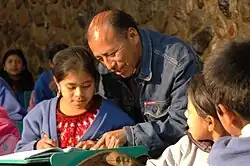 Middle-aged amle teacher helping a young girl as her classmates watch
