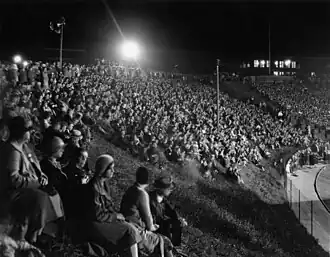 Religious pilgrims sitting on the grass at Creighton Stadium at night.