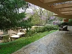A view toward Fallingwater's main house from an outdoor path just outside its guest wing. The path is covered by a canopy. The main house can be seen down the hill.