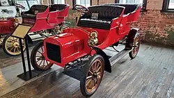 A red-colored, old-fashioned car with two seats and brass fittings