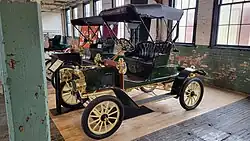 A red-colored, old-fashioned car with three seats and brass fittings