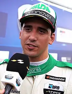 Headshot of di Mauro in racing gear and a baseball cap