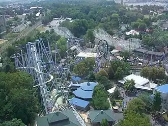 An overhead view of the Great Bear roller coaster among several attractions. The Great Bear roller coaster is left and center of the image, with steel roller coaster SooperDooperLooper located in the middle and left. The Coal Cracker log flume is on the left under the tracks of the Great Bear. The Comet wooden roller coaster is seen in the background, with various paths, buildings, and trees surrounding each attraction.