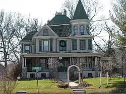 A white house with green roof. It is set back from a lawn and surrounded by bare trees.