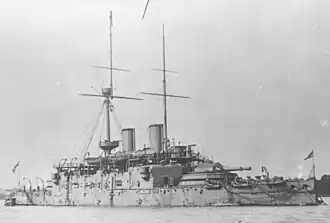 Grey warship with low deck and high superstructure, and barbette armament